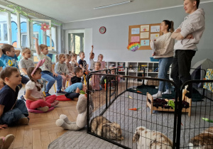 na zdjęciu widać dwie dorosłe osoby stojące przed dziećmi