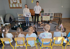 na zdjęciu widać dwie dorosłe osoby stojące przed dziećmi