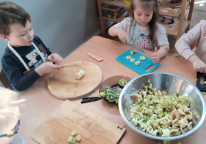 Dzieci kroją sałatkę owocową.