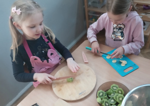 Dziewczynki kroją sałatkę owocową.