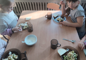 Dzieci jedzą sałatkę owocową.