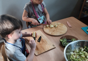 Dzieci kroją sałatkę owocową.