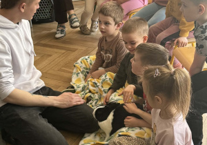 Na zdjęciu mężczyzna rozmawia z dziećmi. Dzieci głaszczą królika.
