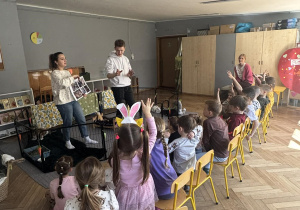 Na zdjęciu widać grupę dzieci podczas warsztatów. Dzieci trzymają rękę w górze, chcąc się zgłosić do odpowiedzi.