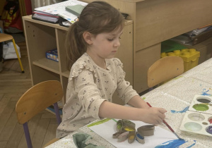 Na zdjęciu widać dziewczynkę malującą farbami swoją pracę.