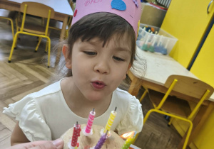 Na zdjęciu widzimy dziewczynkę, która dmucha świeczki na torcie.