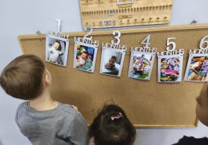 Na zdjęciu widzimy dzieci, które oglądają zdjęcia z różnych etapów życia Solenizantki.