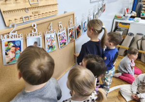 Na zdjęciu widzimy dzieci, które oglądają zdjęcia z różnych etapów życia Solenizantki.