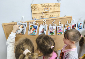 Na zdjęciu widzimy dzieci, które oglądają zdjęcia z różnych etapów życia Solenizantki.