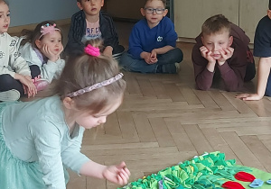 Dziewczynka chowa chrupki do maty przedstawiającej wiosnę