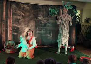 Aktorka trzyma kukiełkę zimę, obok stoi aktor przebrany za drzewo