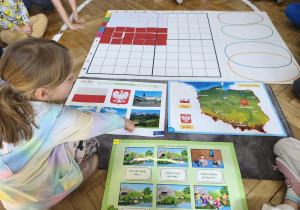 Na zdjęciu widzimy dziewczynkę, która pokazuje na ilustracji dawną stolicę Polski - Kraków.
