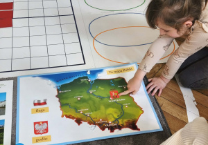 Na zdjęciu widzimy dziewczynkę, która wskazuje na ilustracji herb Warszawy.