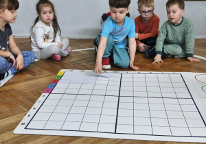 Na zdjęciu widzimy chłopca, który kładzie biały kartonik na odpowiednim polu na macie do kodowania.