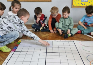 Na zdjęciu widzimy chłopca, który kładzie biały kartonik na odpowiednim polu na macie do kodowania.