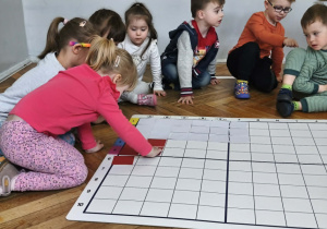 Na zdjęciu widzimy dziewczynkę, która kładzie czerwony kartonik na odpowiednim polu na macie do kodowania.