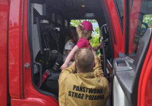 Na zdjęciu widzimy dzieci, które siedzą w wozie strażackim.