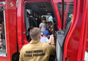 Na zdjęciu widzimy dzieci, które siedzą w wozie strażackim.