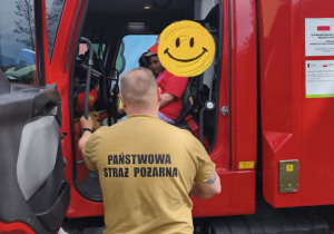 Na zdjęciu widzimy dzieci, które siedzą w wozie strażackim.