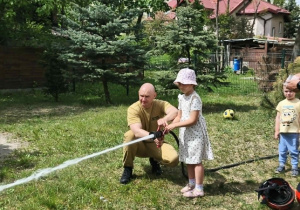 Na zdjęciu widzimy dziecko, które trzyma wąż strażacki i polewa wodę na słupki.