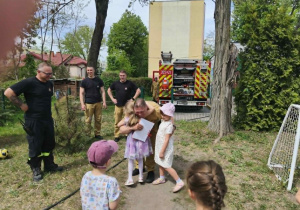 Na zdjęciu widzimy dziecko, które trzyma wąż strażacki i polewa wodę na słupki.