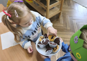 Na zdjęciu widzimy Jubilata, który częstuje dzieci babeczkami.