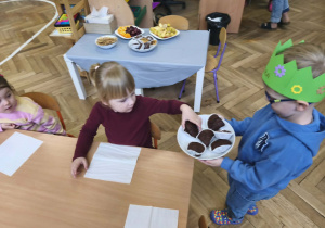 Na zdjęciu widzimy Jubilata, który częstuje dzieci babeczkami.
