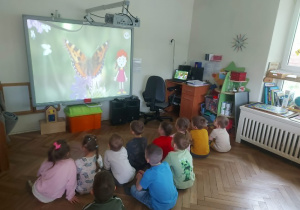 Dzieci zgromadzone przed tablicą, oglądają film edukacyjny o rodzajach motyli
