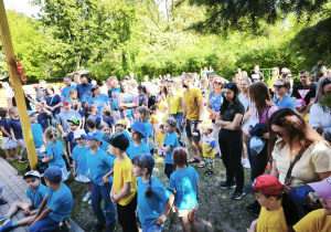 Zdjęcie przedstawia dzieci i rodziców zgromadzonych w ogrodzie.