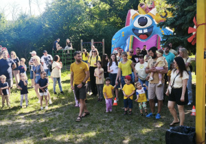 Zdjęcie przedstawia dzieci i rodziców zgromadzonych w ogrodzie.