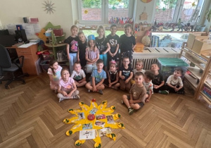Na zdjęciu widać grupę dzieci siedzących przed słoneczkiem urodzinowym. Wśród nich siedzi Jubilatka w koronie.