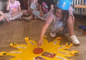 Na zdjęciu dziewczynka wkłada świeczkę w drewniany tort.
