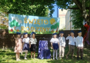 Zdjęcie przedstawia dzieci stojące w półkolu, na tle banera, podczas występu.