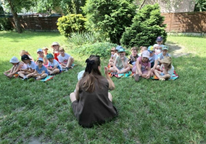 przed kobietą, na trawie siedzi grupa dzieci