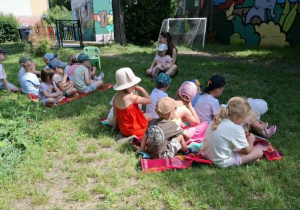 przed kobietą, na trawie siedzi grupa dzieci