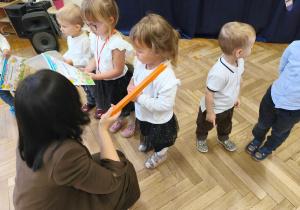 Na zdjęciu kobieta dotyka kredką ramienia dziecka- pasuje je na przedszkolaka.