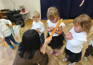 Na zdjęciu kobieta dotyka kredką ramienia dziecka- pasuje je na przedszkolaka.