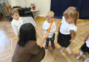 Na zdjęciu kobieta dotyka kredką ramienia dziecka- pasuje je na przedszkolaka.