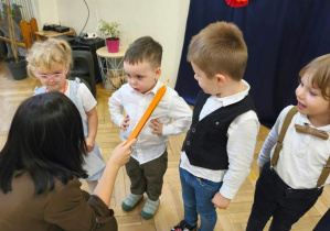 Na zdjęciu kobieta dotyka kredką ramienia dziecka- pasuje je na przedszkolaka.