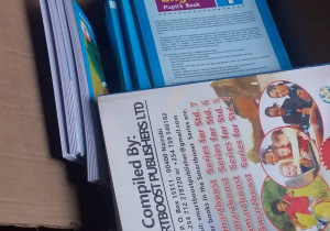 Zdjęcie przedstawia wielkie otwarte pudełko, a wnim mnóstwo książek szkolnych do nauki dzieci w Kenii.