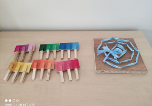 II miejsce- zdjęcie przedstawia dwie pomoce rozwojowe: kolorowe tabliczki i spinacze oraz przeplatanka z wykorzystaniem niebieskiej wstążki i metalowych elementów na drewnianej deseczce