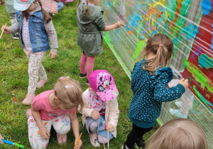 Zdjęcie przedstawia dzieci malujące farbami na folii. Dzieci znajdują się w ogrodzie przedszkolnym.