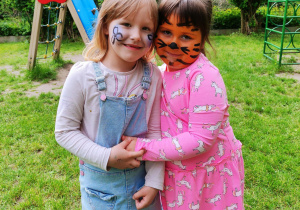 Zdjęcie przedstawia dwie dziewczynki, które mają pomalowane twarze i uśmiechają się do obiektywu.