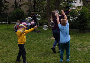 Zdjęcie przedstawia dzieci próbujące złapać fruwające w powietrzu bańki.