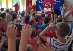 Na zdjęciuna zdjeciu widać, śpiewające dzieci, które maja uniesione do góry ręce na drugim planie widać kobietę siedzącą na fotelu za nią znajduje się granatowo czerwone tło a na nim napisy, przyjaźń, fiends, widać rónież wycięte z papieru drzewo i liście pokolorowane jak flagi Polski i Stanów Zjednoczonych