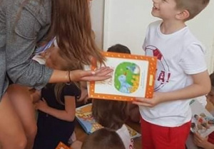 na zdjęciu widać kobietę wręczającą książkę uśmiechniętemu chłopcu, ubranemu w barwy polskiej flagi