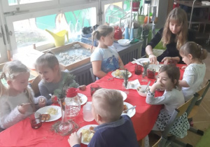 Zdjęcie przedstawia wolontariuszkę i dzieci przy stole wigilijnym.