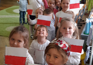 Zdjęcie przedstawia dzieci i wolontariuszkę z polskimi flagami.