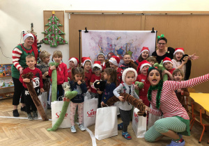 Zdjęcie przedstawia grupę dzieci, nauczycielkę, dyrektora oraz wolontariuszkę pozujących do fotografii. Wszyscy mają w strojach świąteczne akcenty.