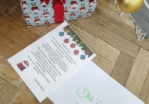 Zdjęcie przedstawia list od Mikołaja leżący pod choinką obok prezentów.